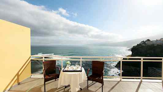 To stoler og et bord med duk står på en terrasse med utsikt over havet. (AI-generert tekst)