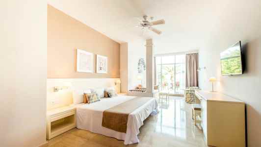 Lyst hotellrom med dobbeltseng og utsikt mot en terrasse. (AI-generert tekst)