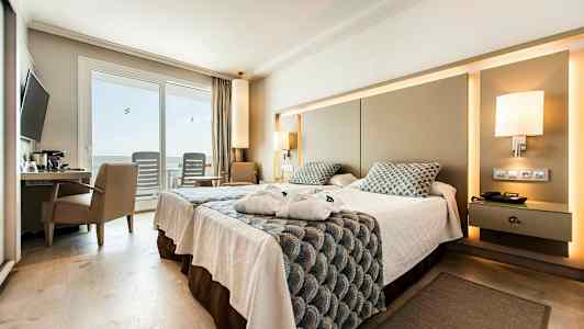 Et hotellrom med en dobbeltseng, skrivebord og stol, samt en terrasse med stoler utenfor glassdører. (AI-generert tekst)