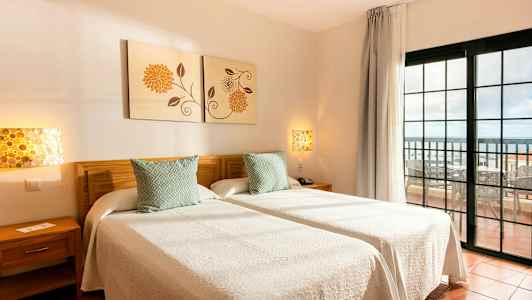 To enkeltsenger med hvitt sengetøy i et rom med utsikt mot en balkong. (AI-generert tekst)