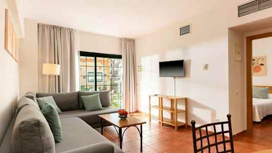 Bilde av en stue med en grå sofa, bord og en TV montert på veggen. (AI-generert tekst)