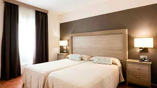 Et soverom med to enkeltsenger, en felles sengegavl og mørke gardiner ved et vindu. (AI-generert tekst)