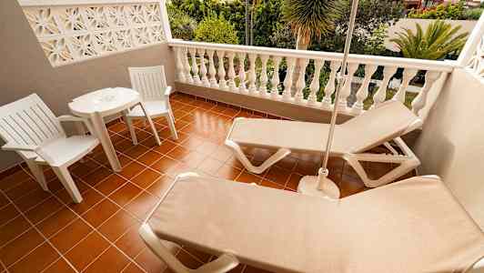 En terrasse med to solsenger, et bord og to stoler med utsikt over grønne omgivelser. (AI-generert tekst)