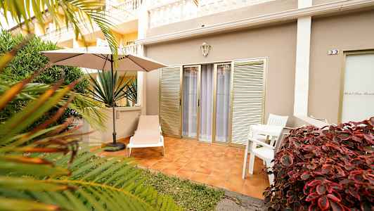 Uteplass med solseng, parasoll og bord med stoler, omgitt av vegetasjon. (AI-generert tekst)