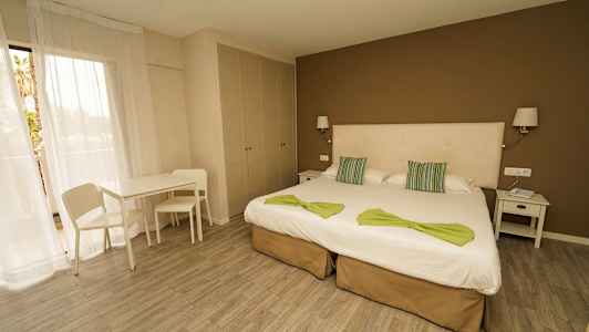 Et hotellrom med to enkeltsenger, nattbord, bord, stoler og et skap. (AI-generert tekst)