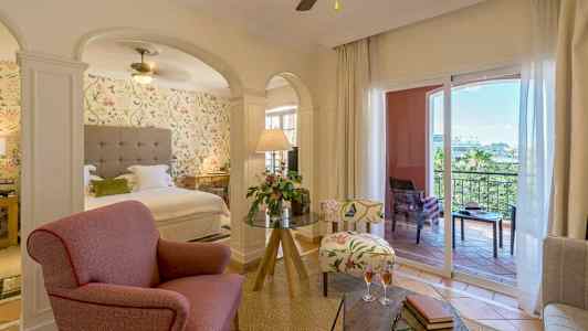 Et hotellrom med sittegruppe, seng og balkong. (AI-generert tekst)