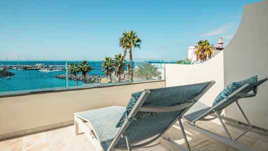 To solsenger på en balkong med utsikt over en havn og sjøen. (AI-generert tekst)