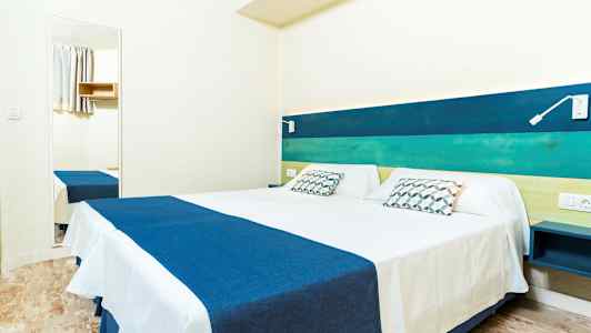 Et dobbeltrom med seng med blått og hvitt sengetøy, hodegavl i blå og grønne nyanser samt veggspeil. (AI-generert tekst)