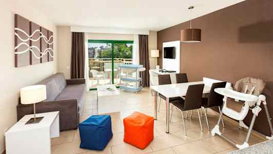 En moderne stue med sofa, spisebord, barnestol og utsikt mot en balkong. (AI-generert tekst)