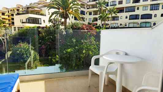 Utsikt fra balkong med hvite plastmøbler og omkringliggende grønne områder. (AI-generert tekst)