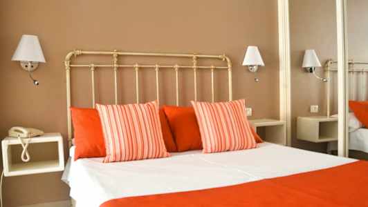 Et hotellrom med en seng kledd i hvite og røde sengeklær, omgitt av vegglamper. (AI-generert tekst)