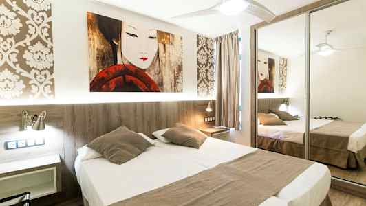 Et hotellrom med en dobbeltseng, speilgarderobe og dekorativ tapet. (AI-generert tekst)