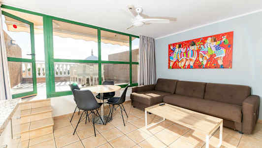 En stue med sofa, spisebord og stoler. I bakgrunnen vises en terrasse med bord og stoler. (AI-generert tekst)