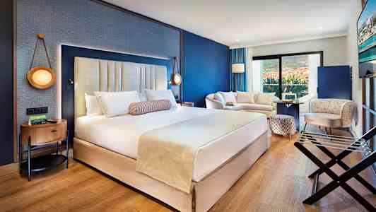 Et moderne hotellrom med en stor dobbeltseng, sittegruppe og balkong. (AI-generert tekst)