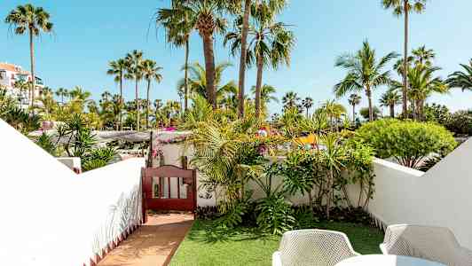 Utsikt fra en frodig hage med palmer og busker, omgitt av hvite vegger. (AI-generert tekst)