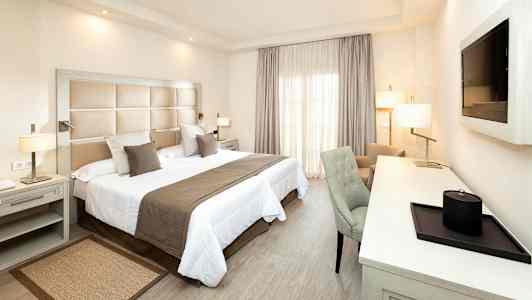 Et hotellrom med en dobbeltseng, skrivebord og stol. (AI-generert tekst)