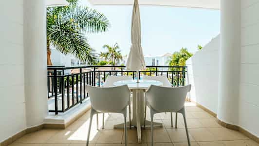 En møblert balkong med utsikt over palmetrær og en bygning. (AI-generert tekst)