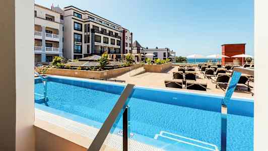 Utsikt over et basseng med solsenger, omgitt av hotellbygninger. (AI-generert tekst)