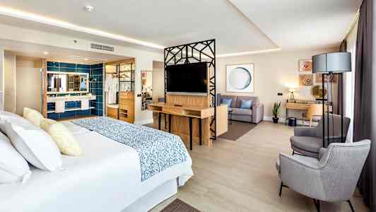 Et hotellrom med en stor seng, sittegruppe og skrivebord. (AI-generert tekst)