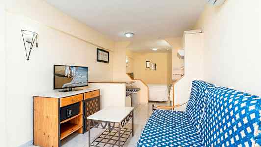 Et studio med en sofagruppe, et bord og en kommode med en TV på. I bakgrunnen er det en seng. (AI-generert tekst)