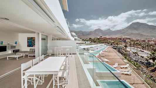 En terrasse med utsikt over bassenger og fjell i bakgrunnen. (AI-generert tekst)