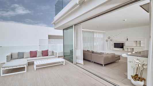 En lys terrasse med sofamøbler og utsikt til en moderne stue med glassvegger. (AI-generert tekst)