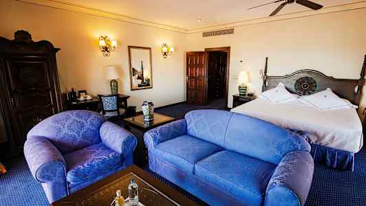 Et hotellrom med en dobbeltseng, to stoler, et bord og en kommode, elegant innredet. (AI-generert tekst)