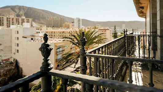 Balkong med detaljerte jerngjerder og utsikt over bybygninger med fjell i bakgrunnen. (AI-generert tekst)