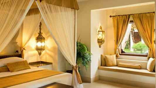 En elegant soveromsinteriør med himmelseng og vindusplass med gullputer. (AI-generert tekst)