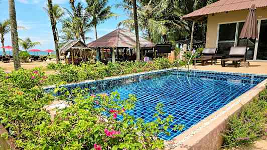 Et basseng omgitt av blomster og planter med palmer og en strand i bakgrunnen. (AI-generert tekst)