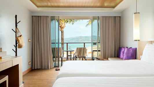 Hotellrom med to senger, skrivebord og balkong med utsikt over stranden. (AI-generert tekst)