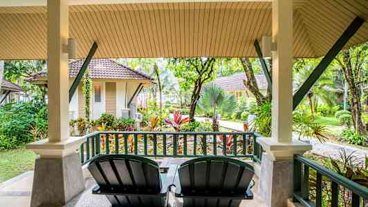 Veranda med to stoler og utsikt over hage og små hus. (AI-generert tekst)