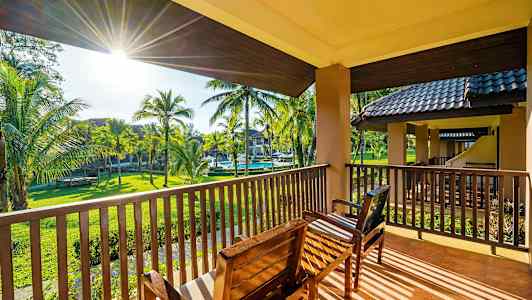 Utsikt fra en balkong med sittemøbler mot en hage med palmer. (AI-generert tekst)