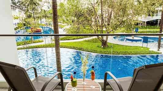 Balkong med to stoler og et bord med drinker, utsikt over basseng og grøntområder. (AI-generert tekst)