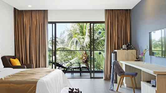 Hotellrom med seng, skrivebord og stoler, samt utsikt mot palmer gjennom en glassdør. (AI-generert tekst)