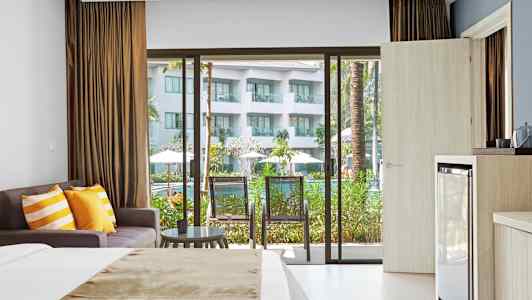 Hotellrom med seng, sofa og balkong med utsikt mot bassengområde. (AI-generert tekst)