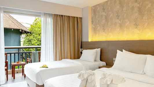 To oppredde enkeltsenger med dekorative håndklær og blomster. Utsikt mot en møblert balkong med grønt og bygning. (AI-generert tekst)