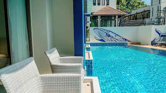 To hvite stoler står på en terrasse ved siden av et svømmebasseng. På veggen ved bassenget er det blå malerier av hvaler. (AI-generert tekst)