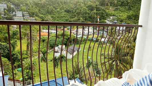 En balkong med utsikt over en grønn dal og bygninger. (AI-generert tekst)