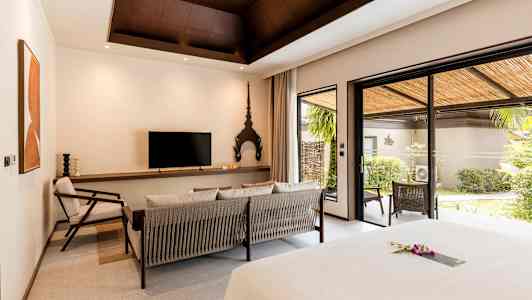 Et hotellrom med moderne innredning, en sittegruppe, en TV, og store glassdører som fører til en frodig terrasse. (AI-generert tekst)