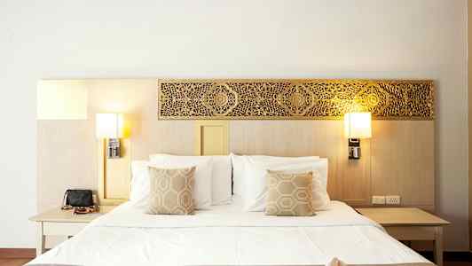 En oppredd seng med pynteputer, flankert av nattbord og vegglamper. (AI-generert tekst)