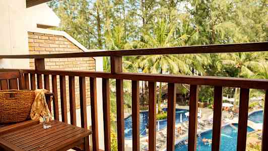 Utsikt fra en balkong mot et basseng og omkringliggende trær. (AI-generert tekst)