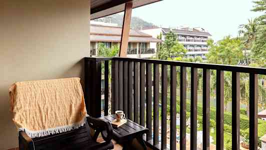 En balkong med en stol, et bord og utsikt over grøntområder og bygninger. (AI-generert tekst)