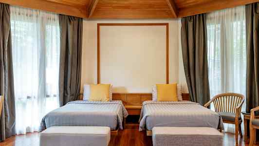 Hotellrom med to enkeltsenger, tremøbler og store vinduer med gardiner. (AI-generert tekst)