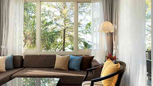 Stue med sofa og puter foran vinduer med utsikt mot grøntområde. (AI-generert tekst)