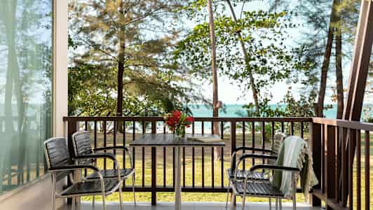 Utsikt fra en veranda med bord og stoler, med havet og trær i bakgrunnen. (AI-generert tekst)