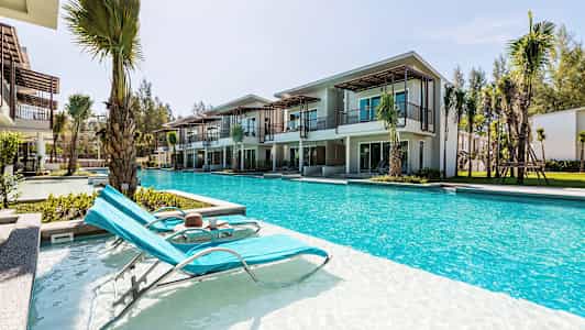 Bilde av solsenger ved et basseng foran moderne ferieboliger. (AI-generert tekst)