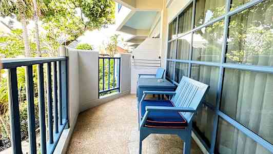 Bilde av en balkong med to blå stoler, bord og utsikt mot trær og grøntområder. (AI-generert tekst)