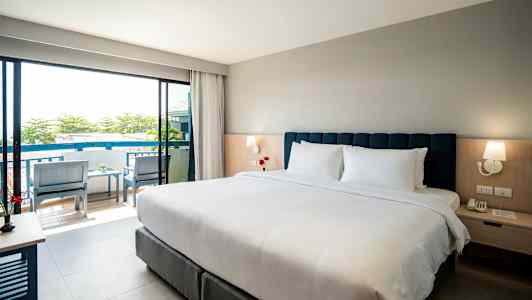 Hotellrom med dobbeltseng, nattbord og utsikt mot balkong. (AI-generert tekst)