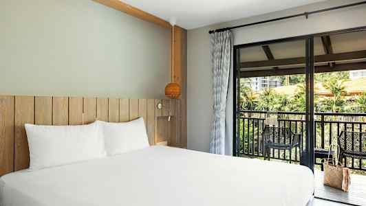 Bilde av et hotellrom med tremøbler og en seng med hvite laken. En balkong med utsikt er utenfor. (AI-generert tekst)